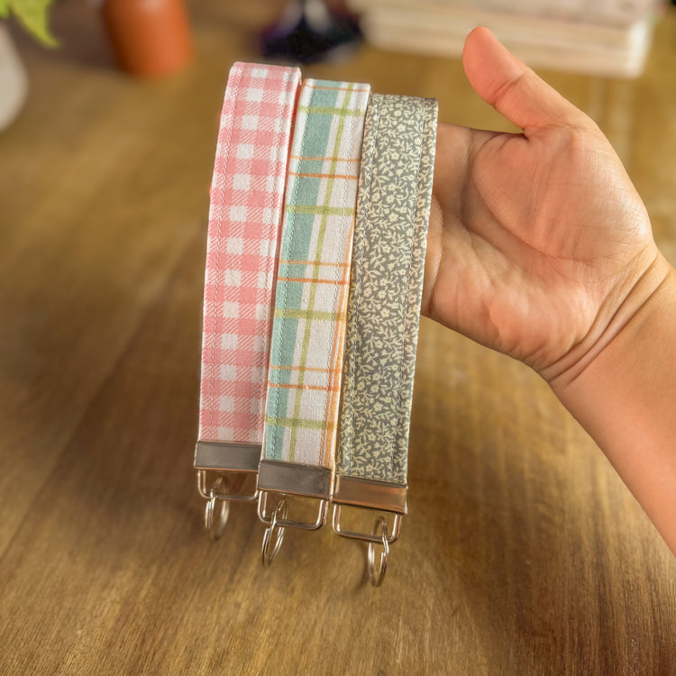 Hand holding a set of colorful fabric keychains on a wooden surface