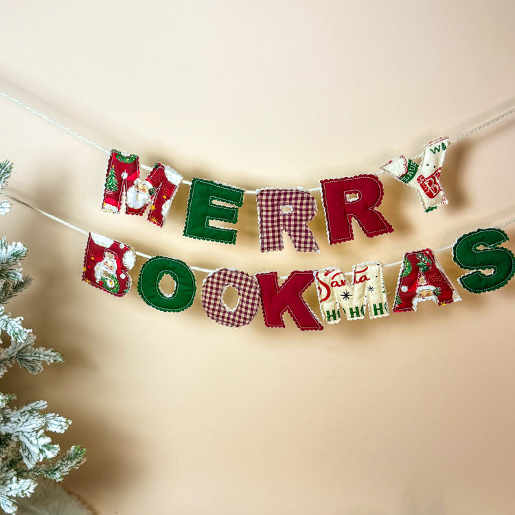 Simple clean shot of the Merry Bookmas banner hanging with a frosted Christmas tree beside it.