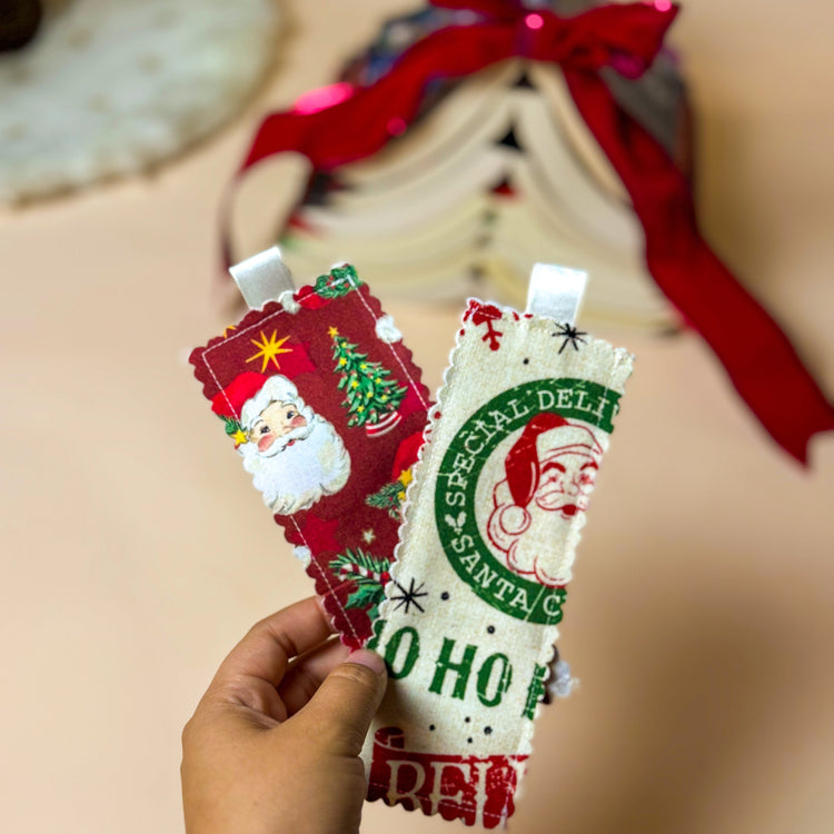 Two Christmas-themed bookmarks held by a hand with a blurred background.