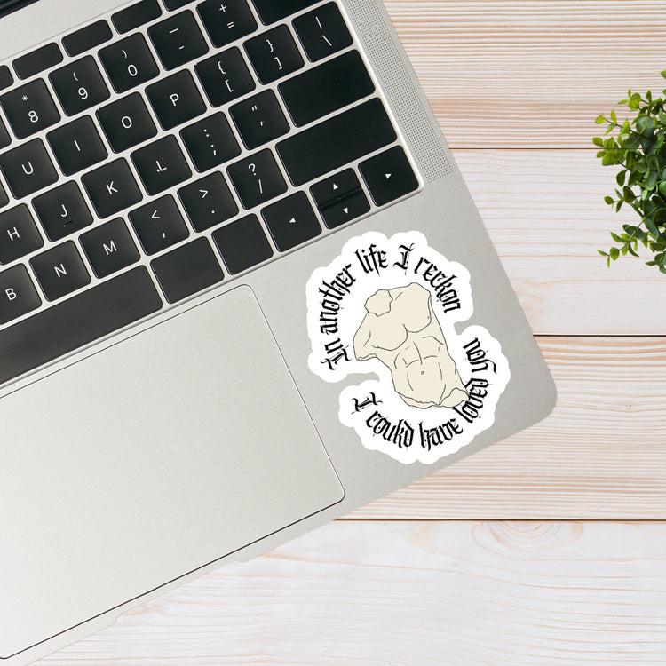 Sticker placed on a silver laptop beside a small plant.