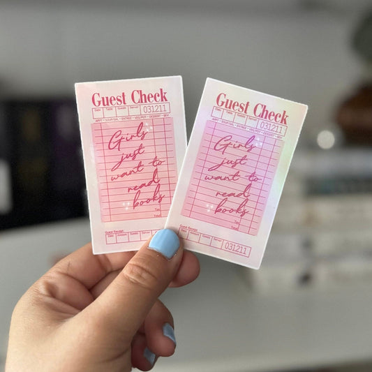 Hand holding two holographic “Girls Just Want to Read” stickers with pink guest check design