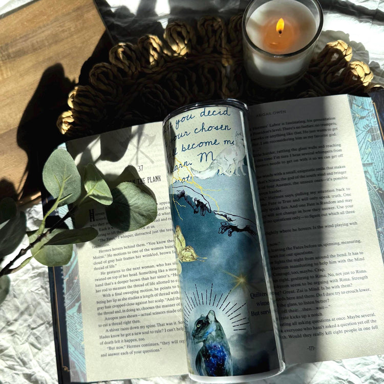 20 oz insulated tumbler standing upright with divine hand artwork, stars, and blue skies, styled with moody fantasy book props and candlelight.