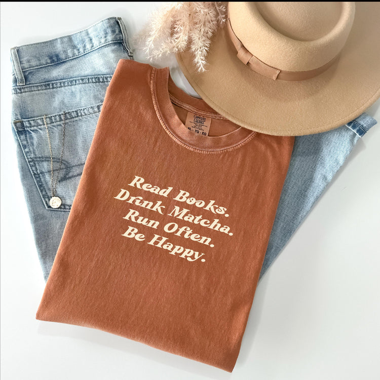 Read Books Drink Matcha Run Often Be Happy tee in Yam, styled with books and cozy props.