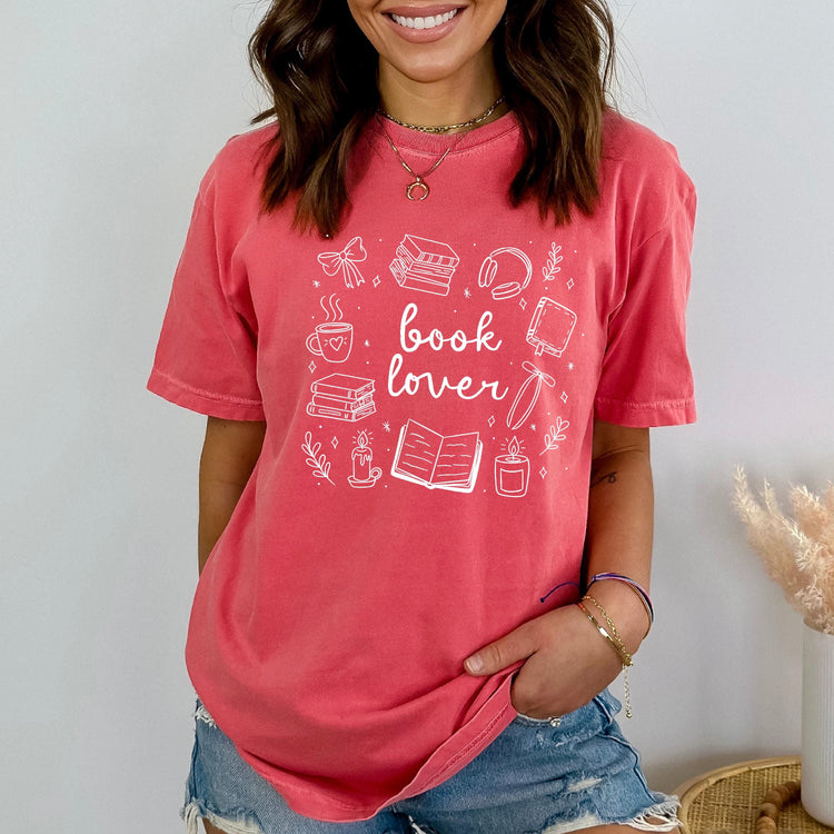 A person wearing a pink oversized t-shirt with 'book lover' text and various literary illustrations, such as books and coffee cups, on it.