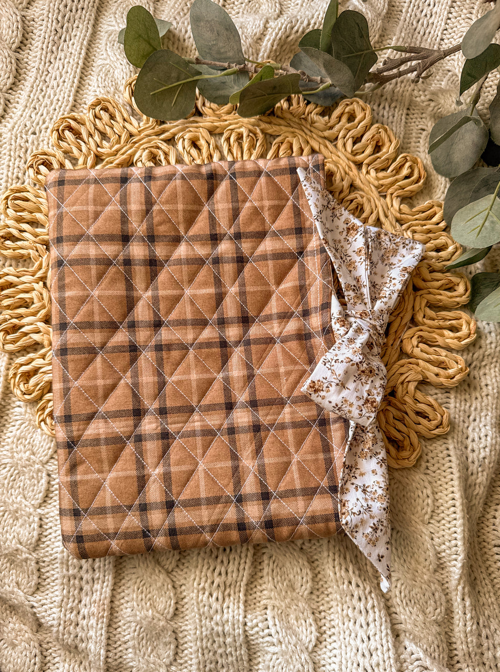 Quilted brown and beige plaid blanket on a textured surface with greenery.