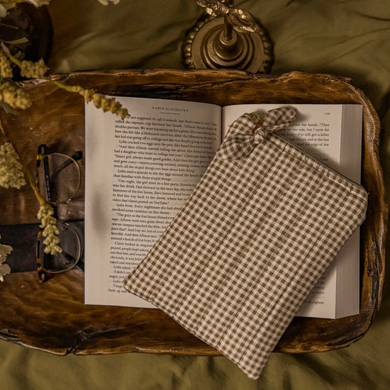 Open book with a checkered fabric kindle case, a wooden tray, surrounded by candles and flowers.