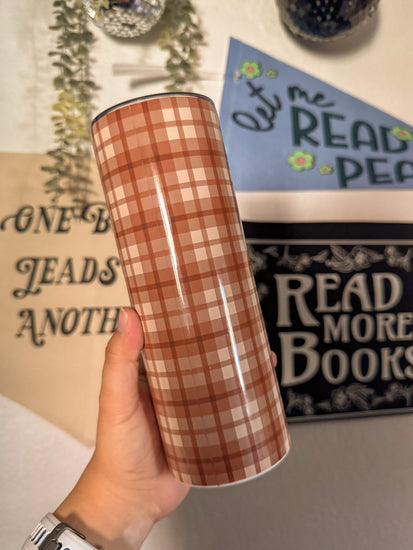 Plaid-patterned tumbler held by a hand with decorative background