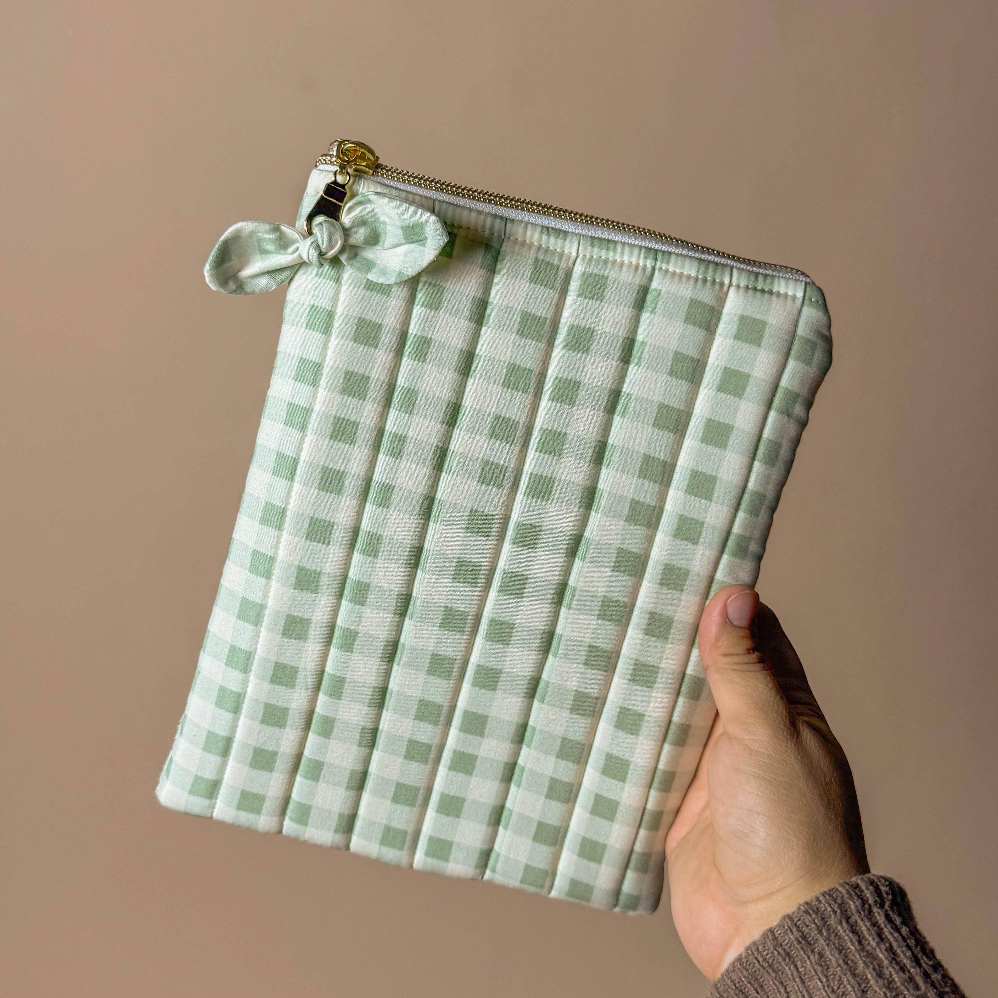 Hand holding a green checkered kindle pouch against a beige background