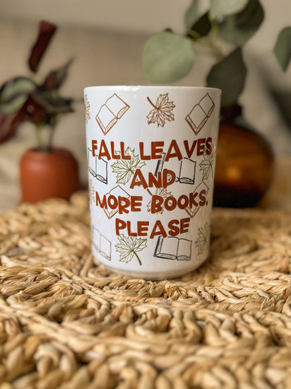 Ceramic mug with 'Fall leaves and more books please' text on a woven mat.