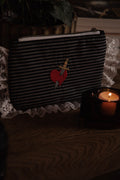 Black striped pouch with a red heart and dagger design on a textured surface with a candle.