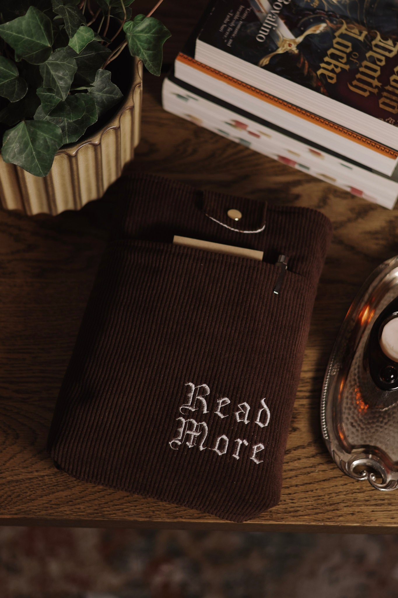 Dark brown book sleeve with 'Read More' text on a wooden surface with books and a plant.