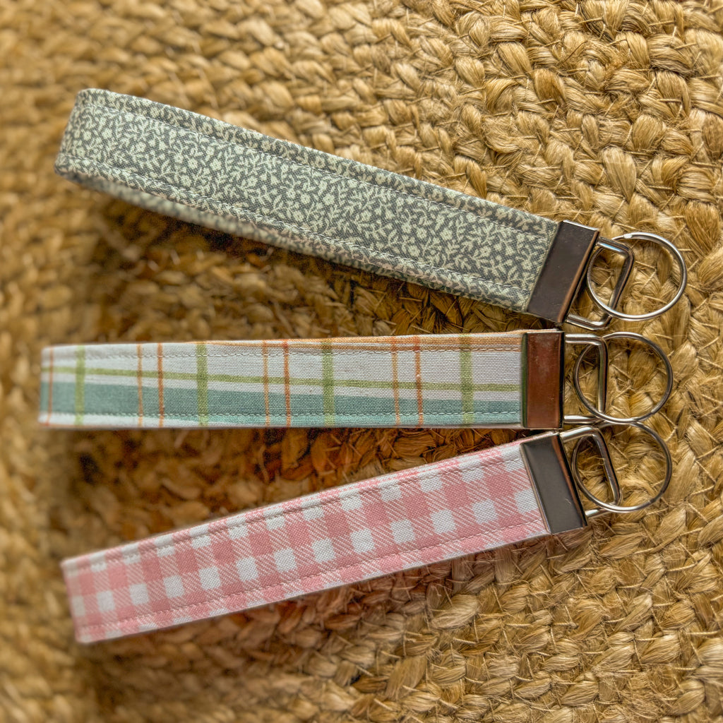 Three fabric keychains with metal clasps on a woven surface
