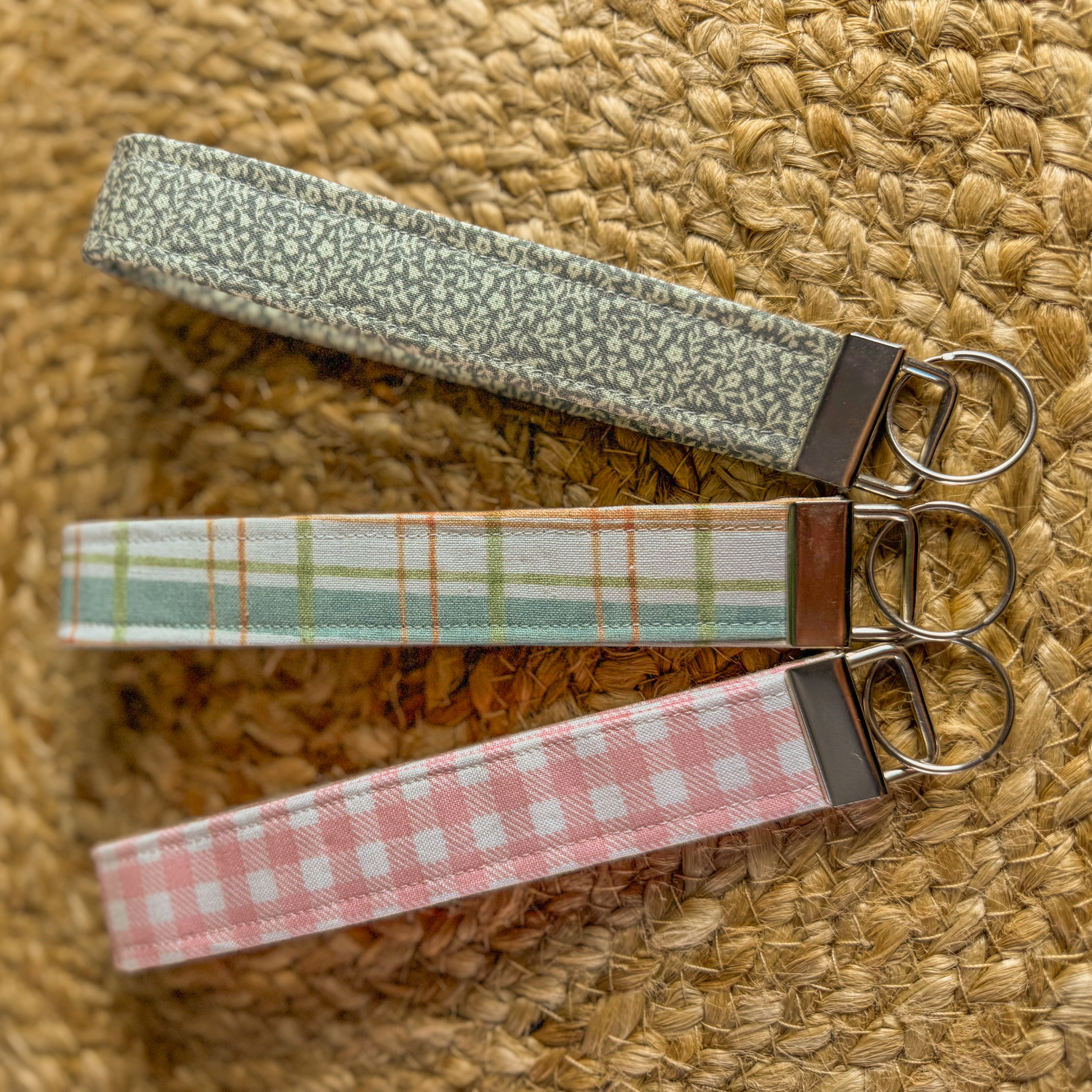 Three fabric keychains with metal clasps on a woven surface