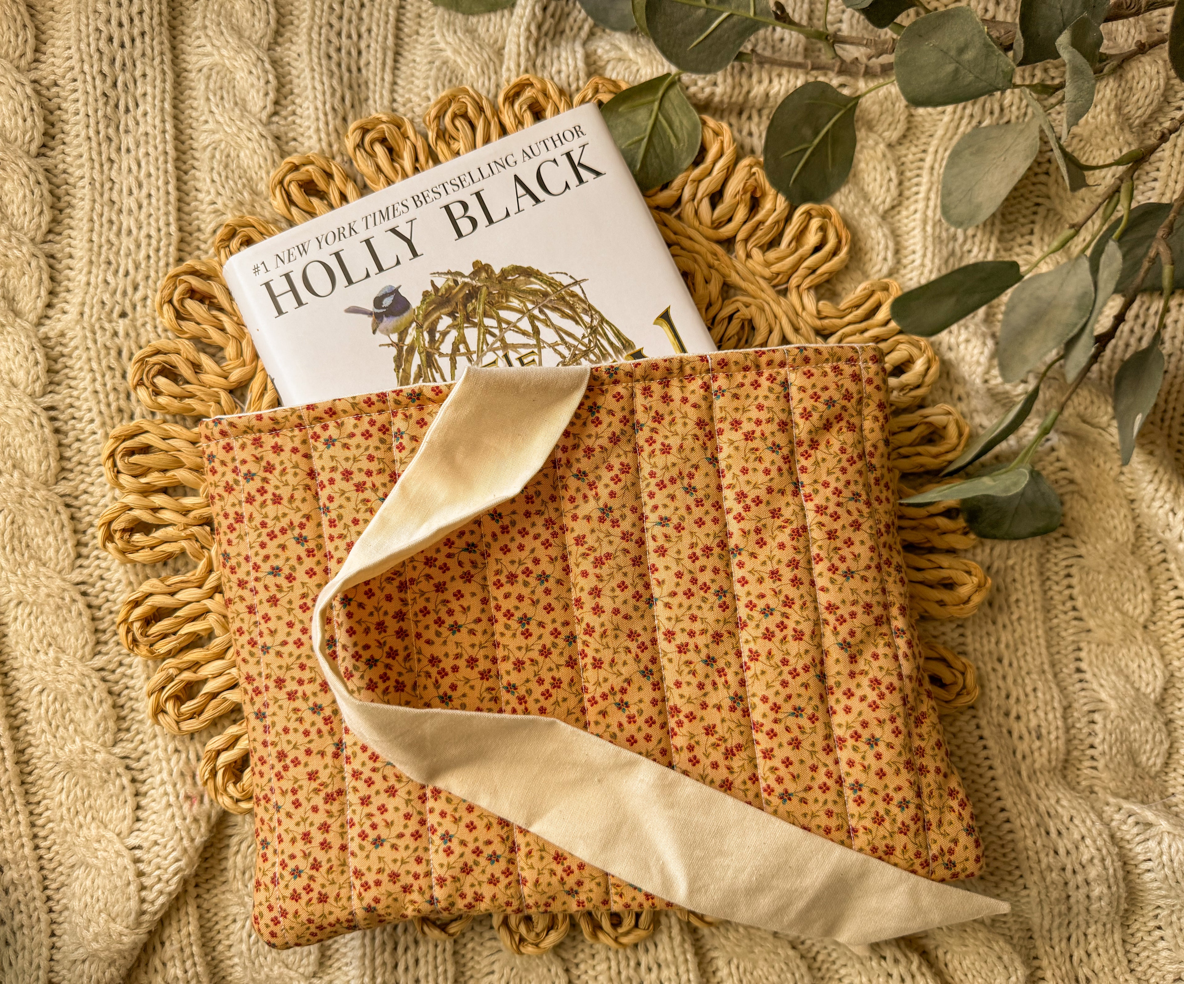 Fabric pouch with a book titled 'Holly Black' on a textured surface with greenery.