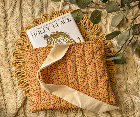 Fabric pouch with a book titled 'Holly Black' on a textured surface with greenery.