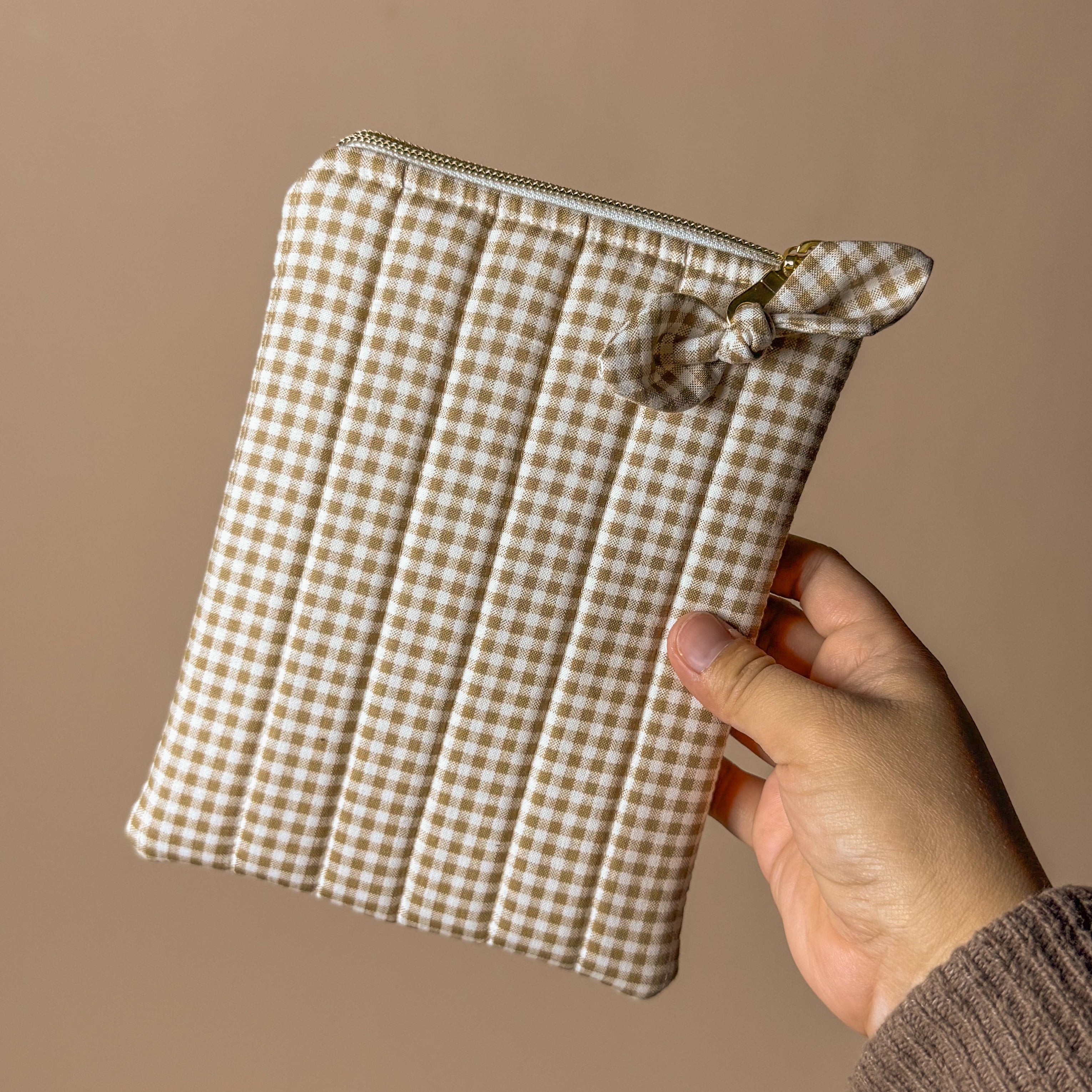 Hand holding a small checkered pouch against a plain background