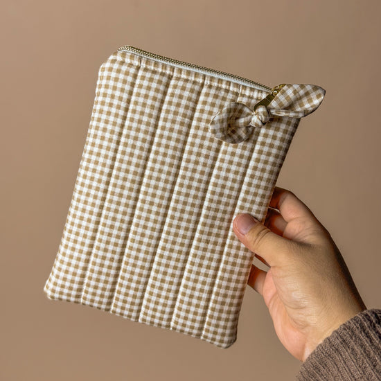 Hand holding a small checkered pouch against a plain background