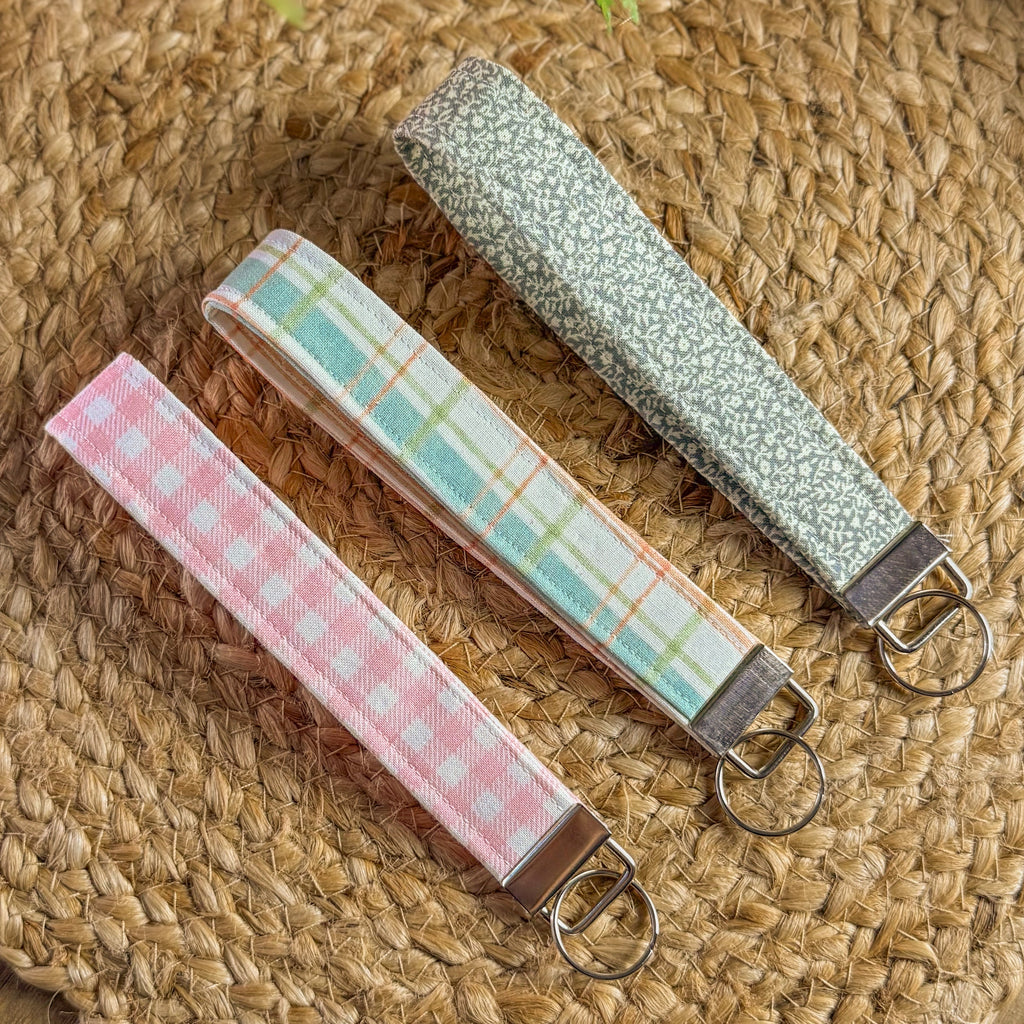Three fabric keychains with different patterns on a woven surface