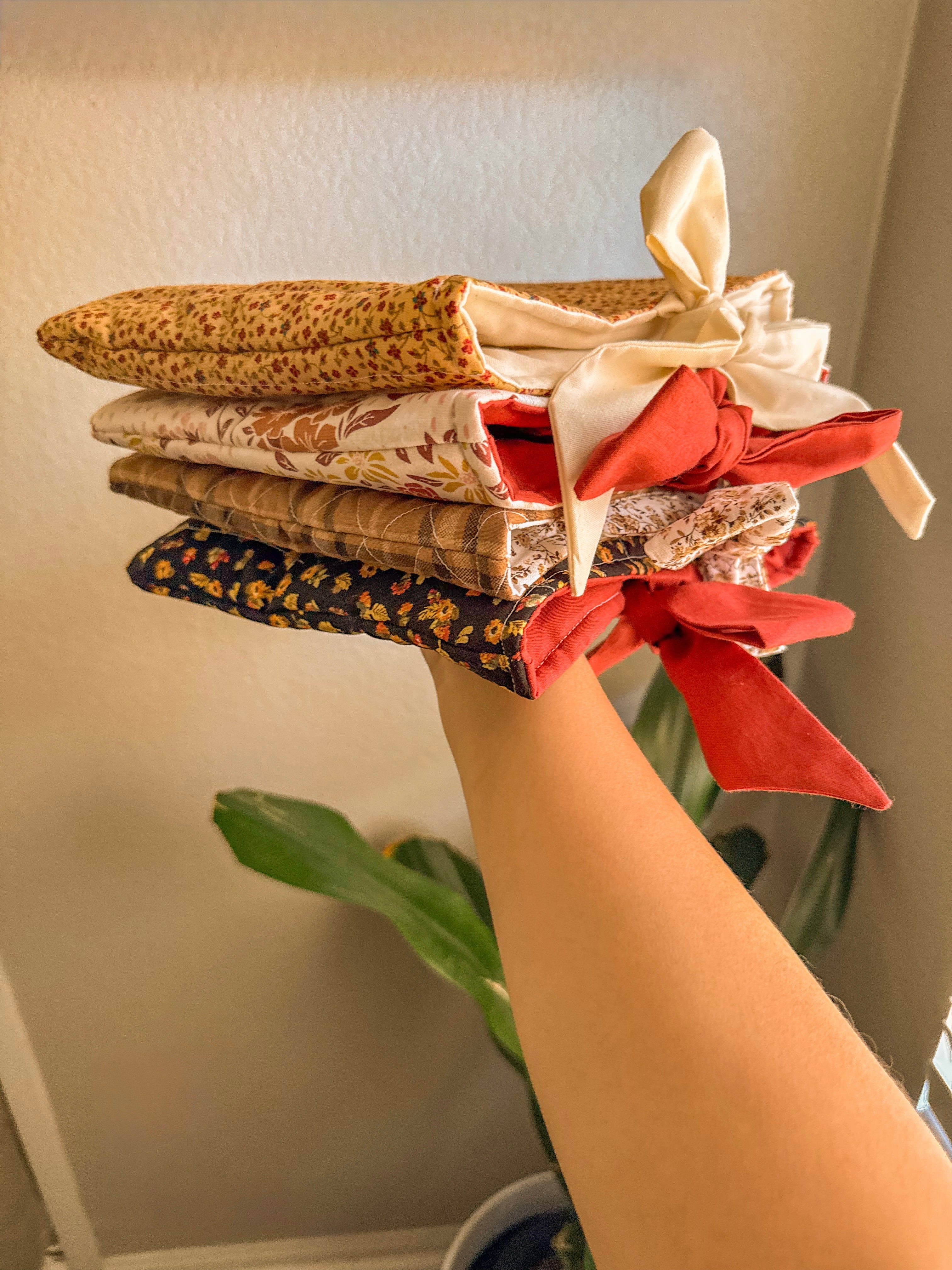 Stack of patterned quilted bow book sleeves held by a hand with a decorative bow against a neutral background