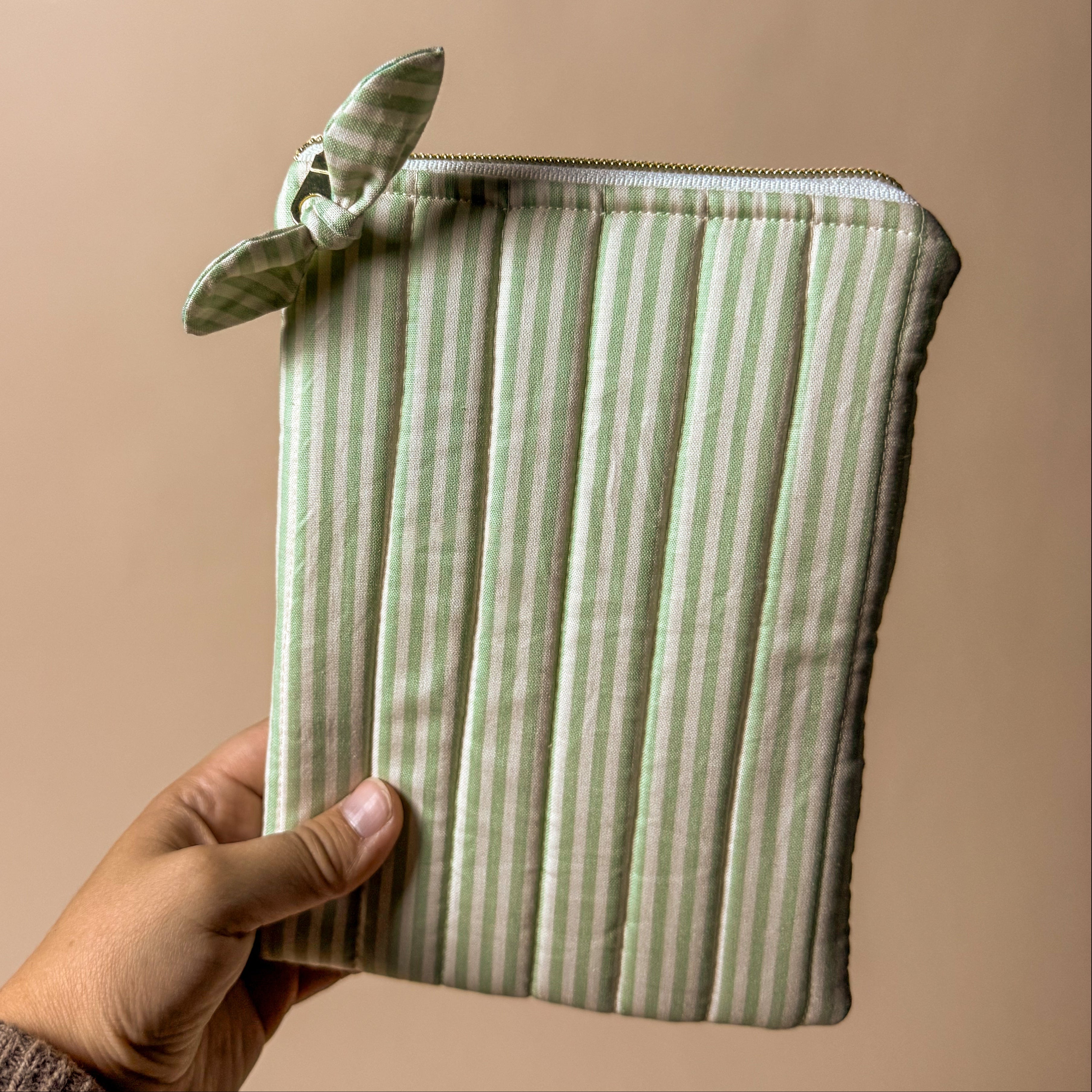 Hand holding a green striped kindle pouch against a beige background