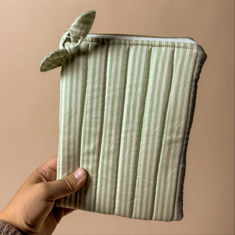 Hand holding a green striped kindle pouch against a beige background