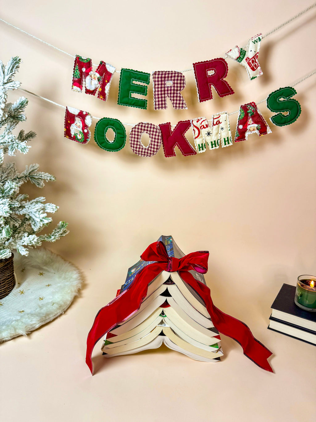 Handmade Merry Bookmas fabric banner hanging above a cozy holiday book scene with a book tree and candle.