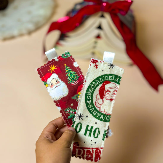Two Christmas-themed  bookmarks held by a hand with a blurred background.