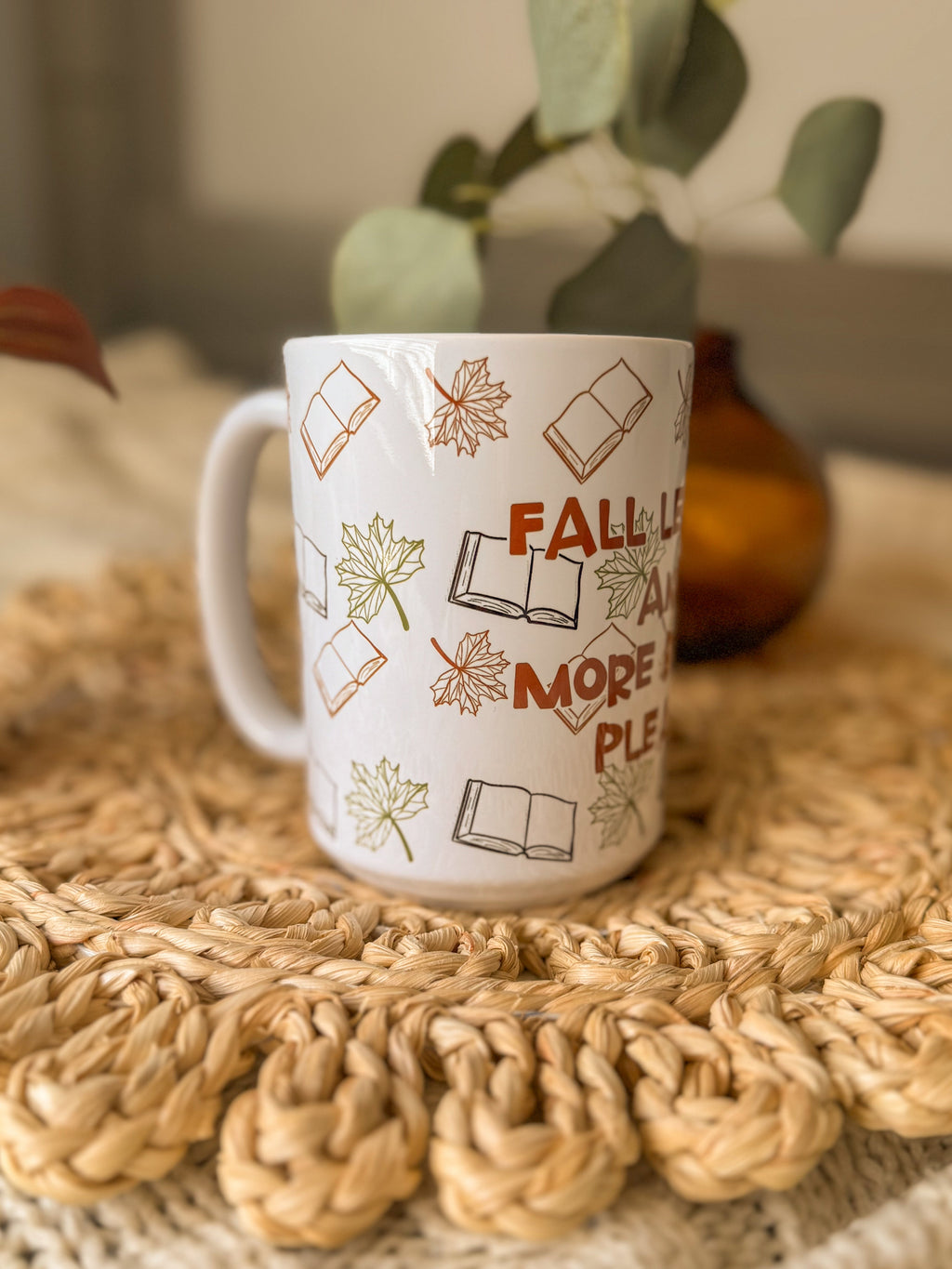 White mug with autumn-themed design on a woven mat with plants in the background