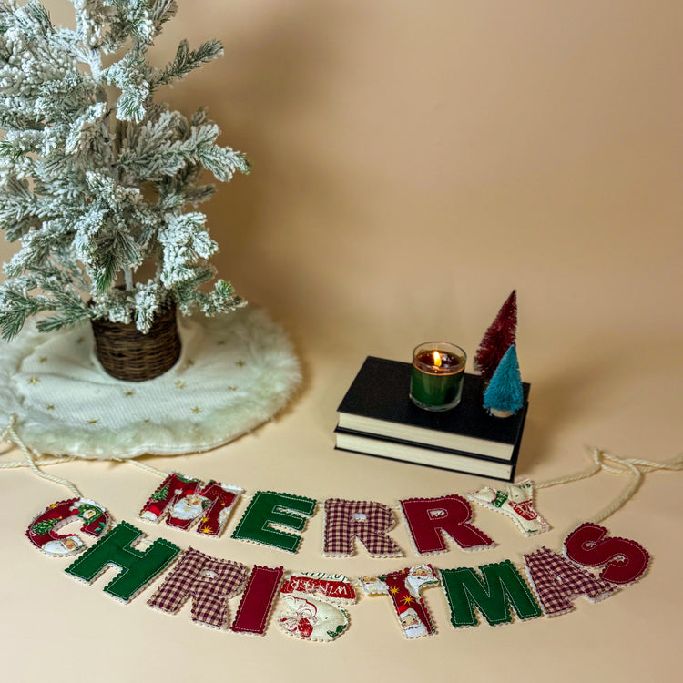 Decorative Christmas scene with a small tree, books, candle, and 'Merry Christmas' sign on a beige background.