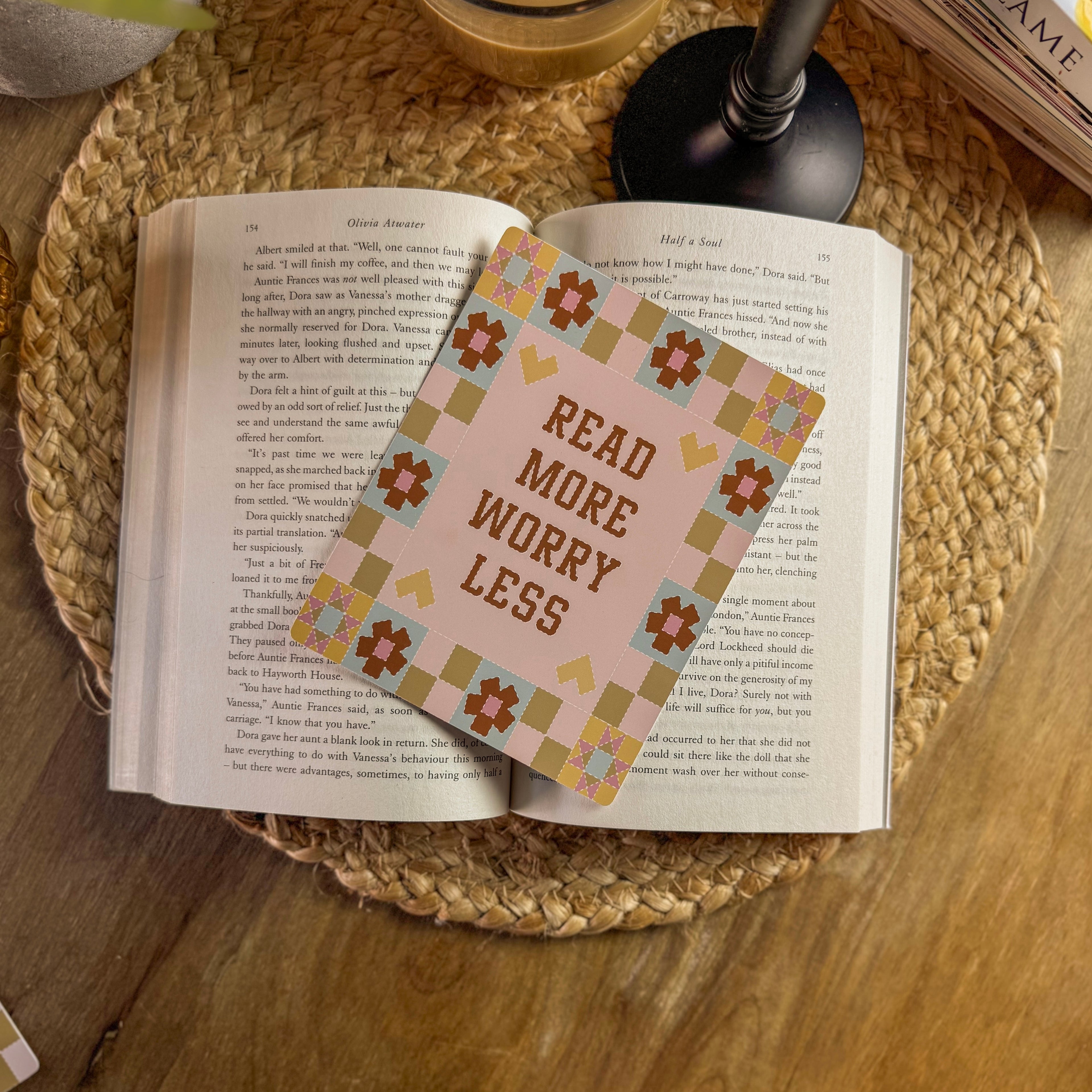 Open book with a decorative e reader insert reading 'Read More Worry Less' on a woven mat.