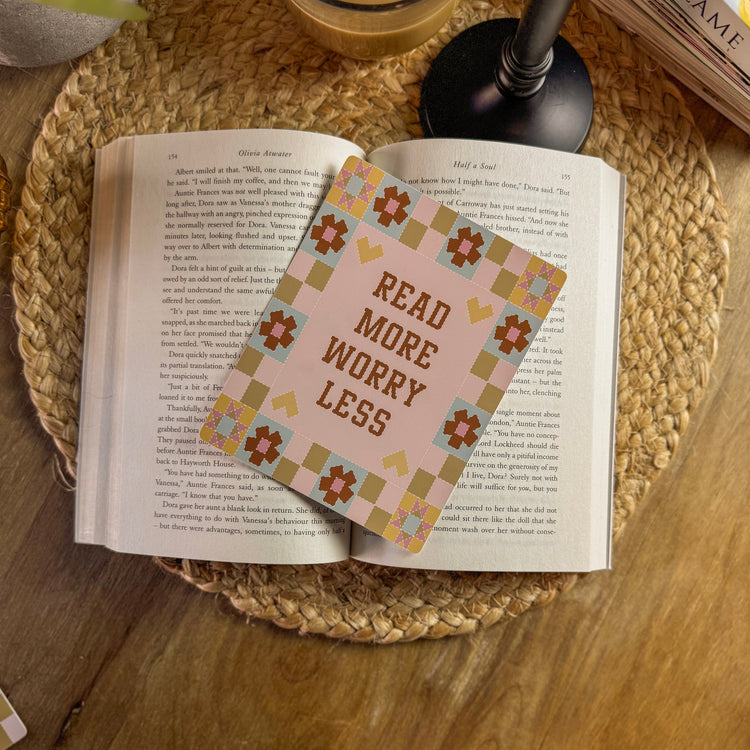 Open book with a decorative e reader insert reading 'Read More Worry Less' on a woven mat.