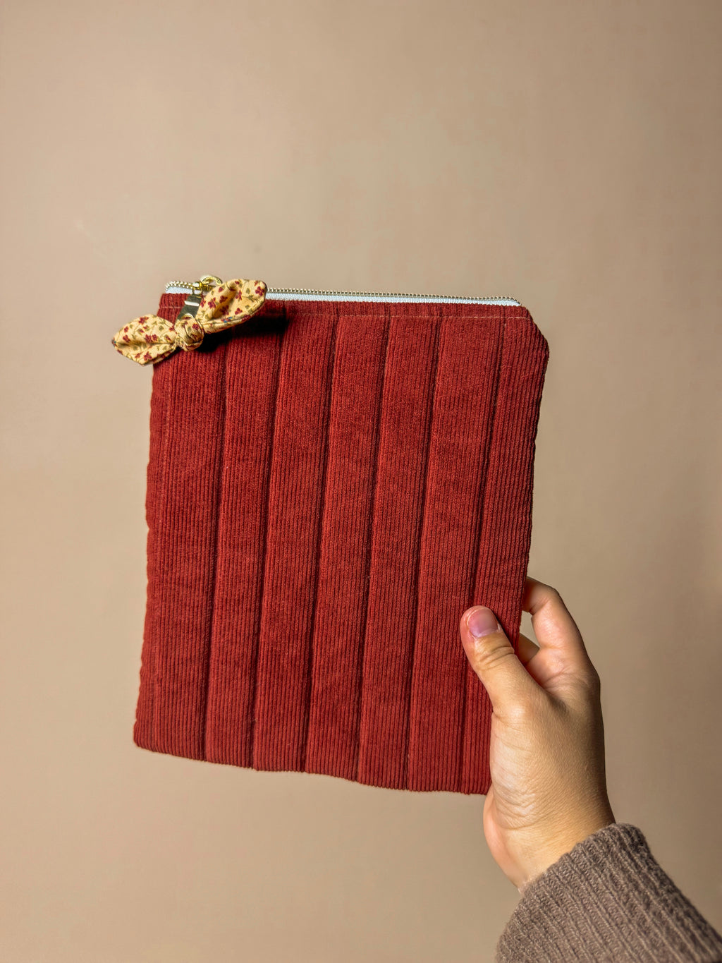 Red corduroy kindle sleeve held by a hand against a beige background