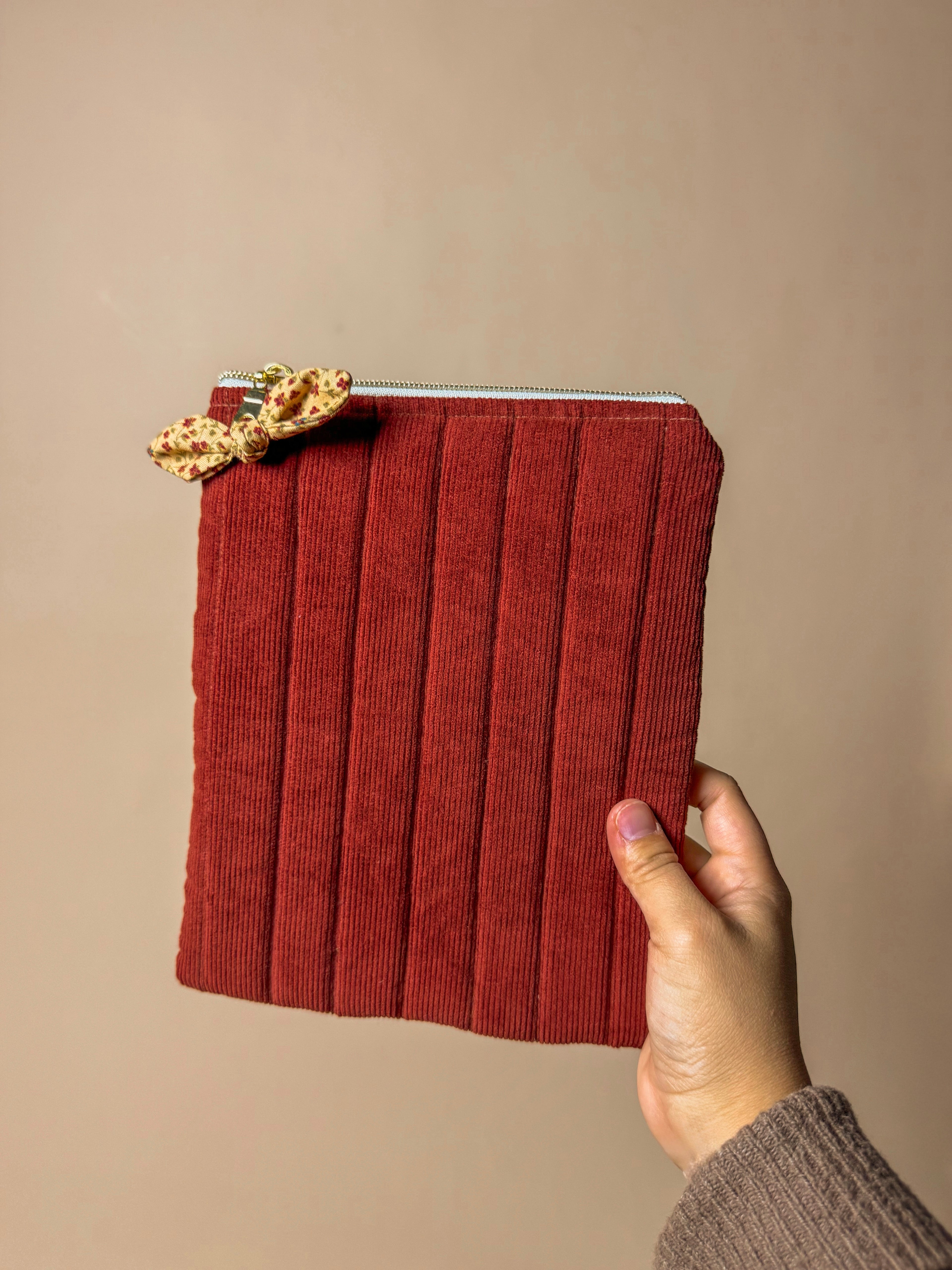 Red corduroy kindle sleeve held by a hand against a beige background
