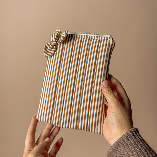 Striped tech  pouch held by a person against a beige background