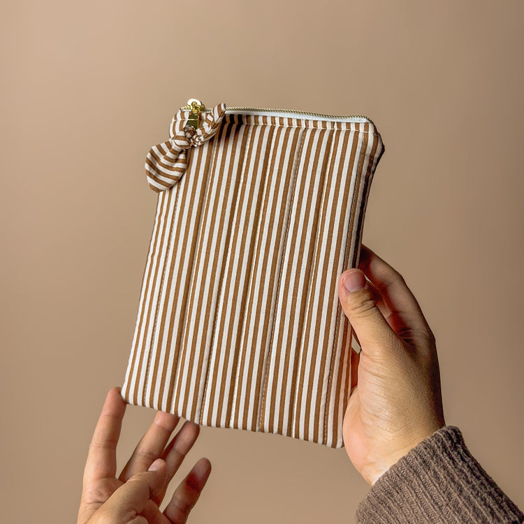 Striped tech  pouch held by a person against a beige background