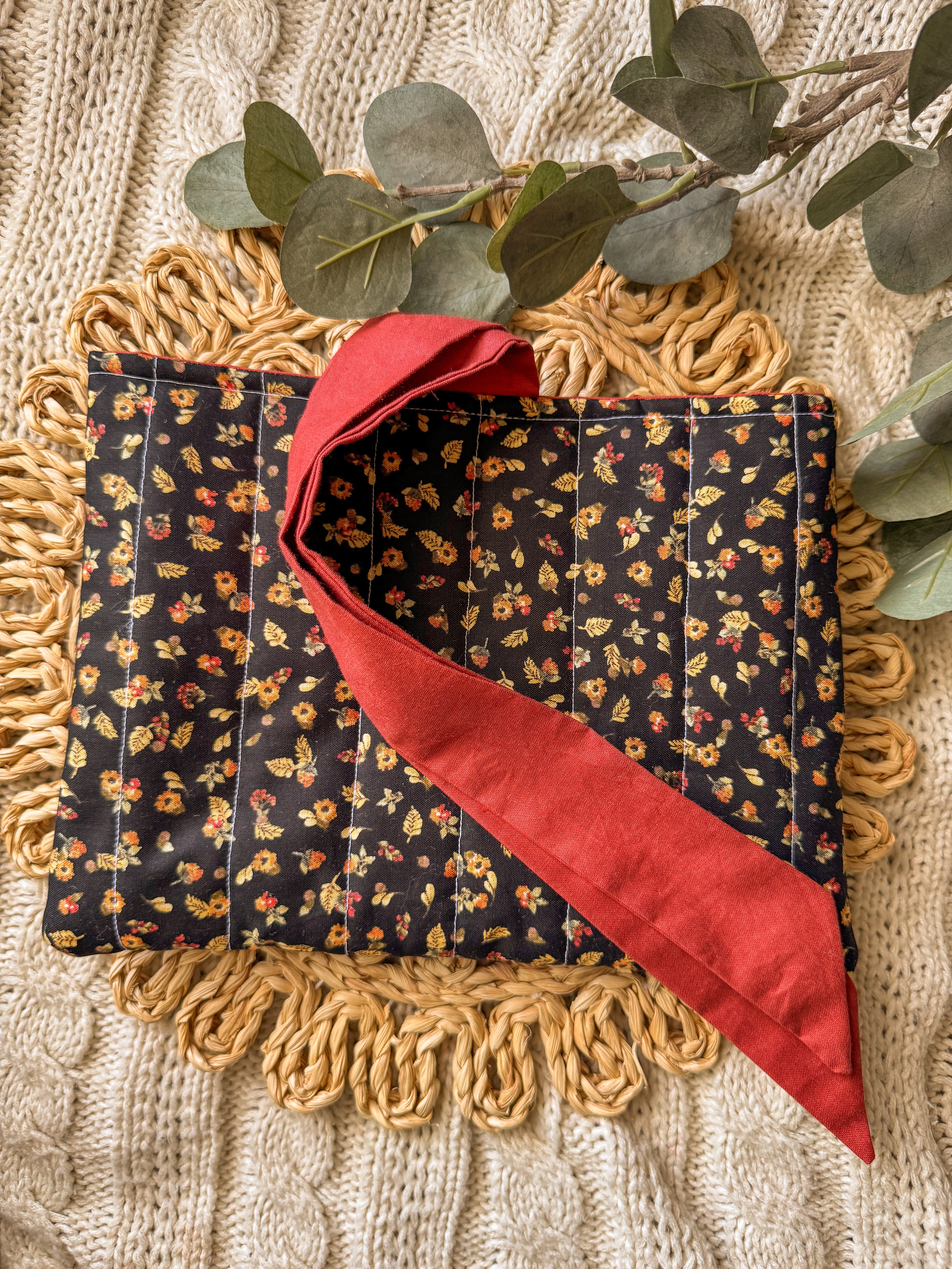 Fabric with floral pattern and red border on a textured surface with eucalyptus leaves.