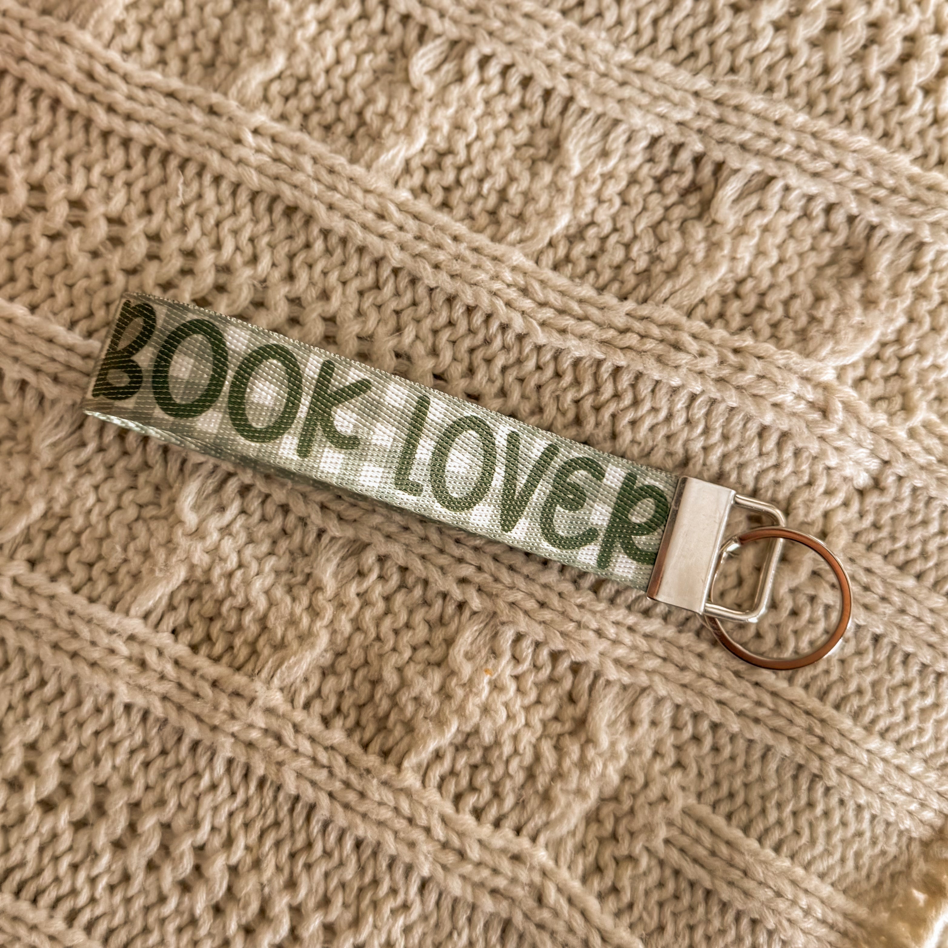 Close up of Green key fob, background is green gingham and the text "BOOK LOVER" in a darker green is written on top. 