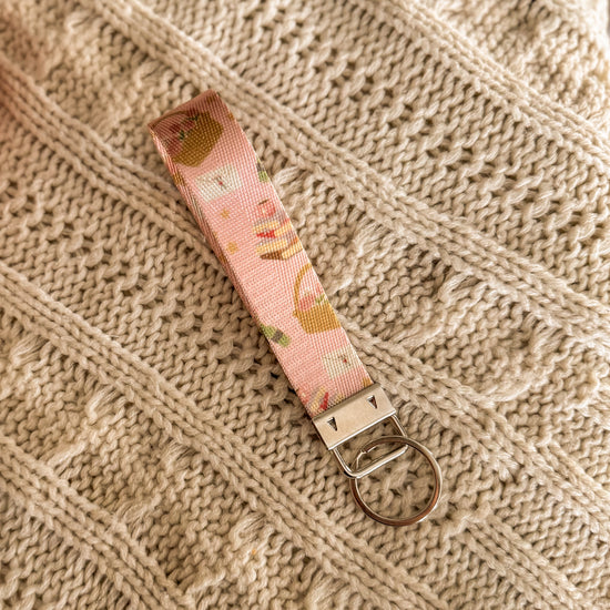 Pink key fob with images of stack of books, picnic baskets, love letters and a wine bottle .