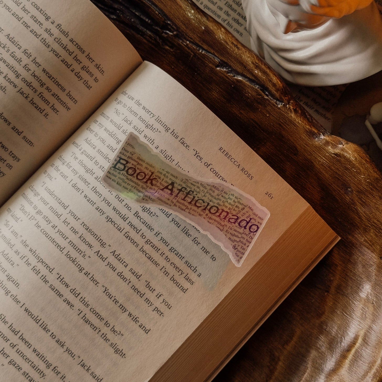Holographic "Book Aficionado" sticker resting on the pages of an open vintage book, showing the intricate design and rainbow shimmer.