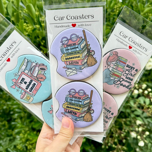 A collection of three Bookish Girlies Car Coasters sets featuring 'Reader Girl', 'Kindle Girlie', and book stack designs, displayed against a natural green background.