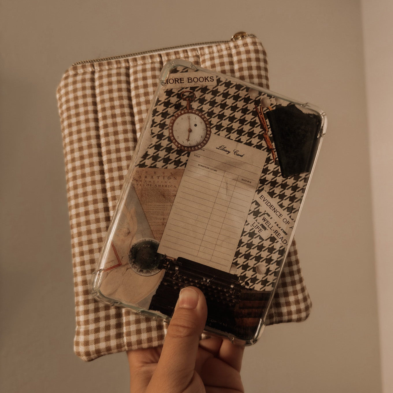 Hand holding a Kindle with a Dark Academia vintage collage insert featuring a library card and houndstooth pattern, styled with a neutral checkered book sleeve.