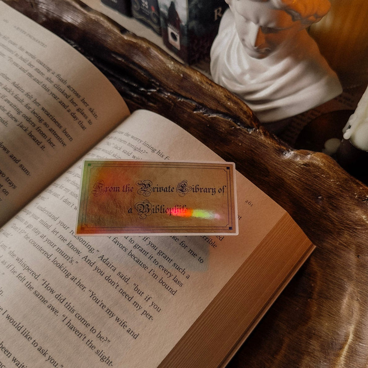 Holographic 'From the Private Library of a Bibliophile' sticker on an open book, styled with a candle and classical bust for a dark academia aesthetic