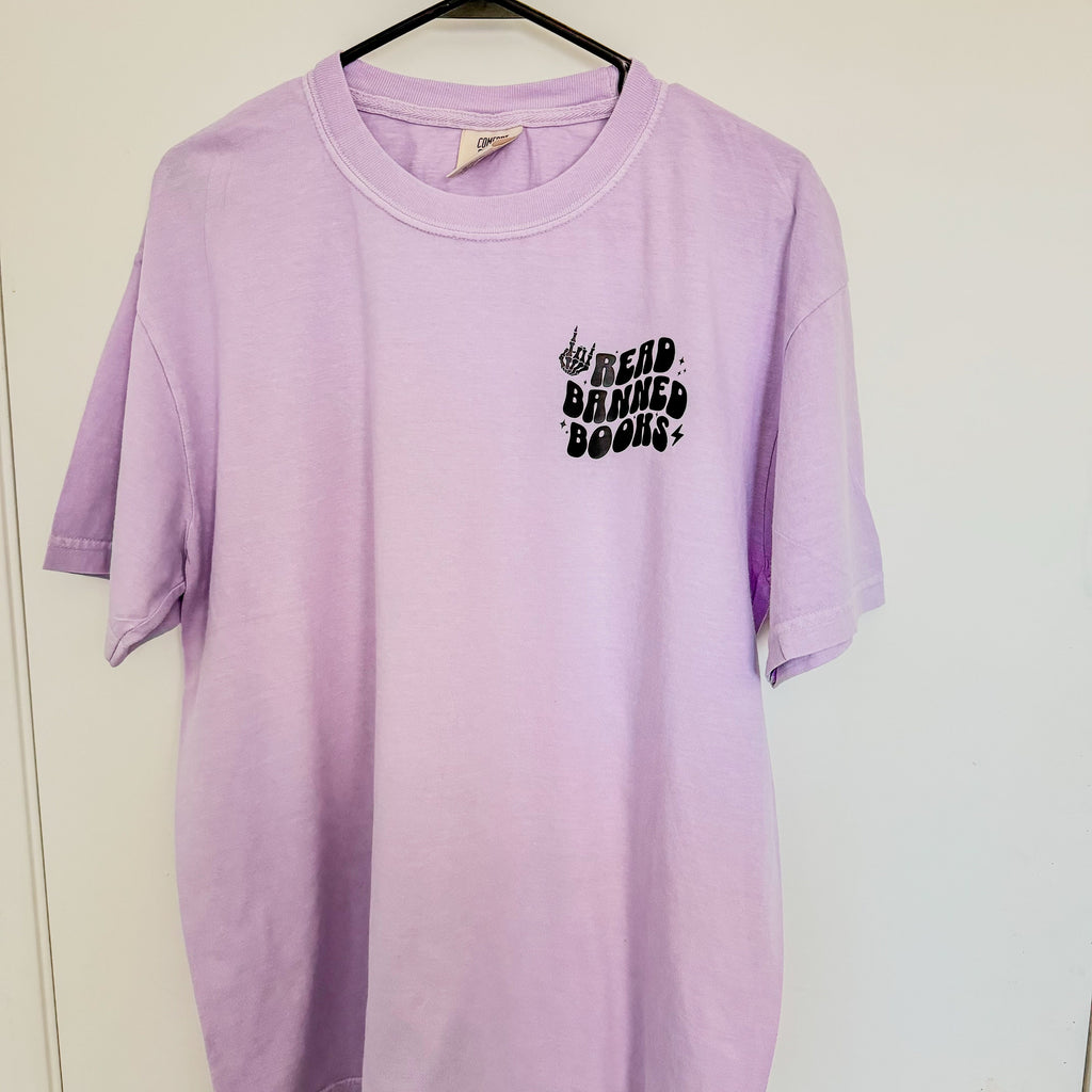 Lavender Read Banned Books tee with front pocket and wavy lettering, styled with books and cozy accents.