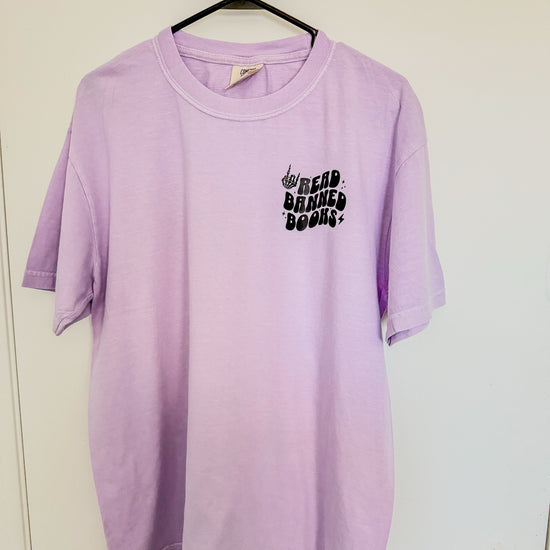 Lavender Read Banned Books tee with front pocket and wavy lettering, styled with books and cozy accents.