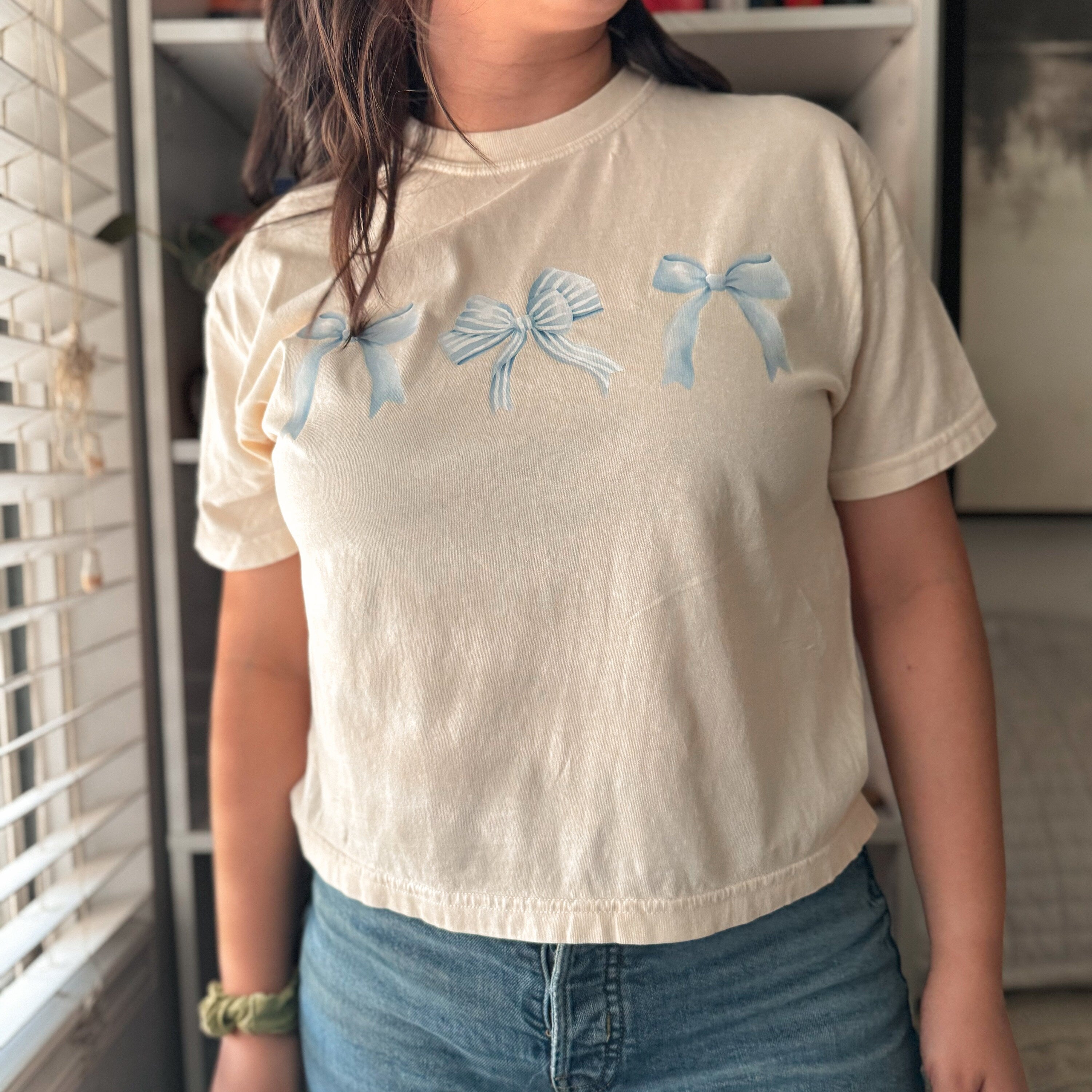 Ivory Coquette Bows cropped tee with blue bows, styled with books and cozy reading props.