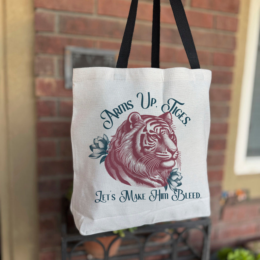 A white polyester tote bag with black straps featuring a red illustration of a tiger's head and the text 'Paws Up, Tiges. Let's Make Him Bleed.