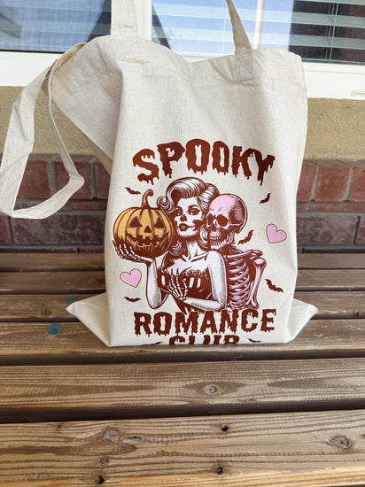 This image features a stylish Spooky Retro Vintage Tote Bag, designed with a nostalgic aesthetic perfect for romance book enthusiasts. The tote displays a whimsical graphic of a skeleton couple embracing, with the woman holding a pumpkin.