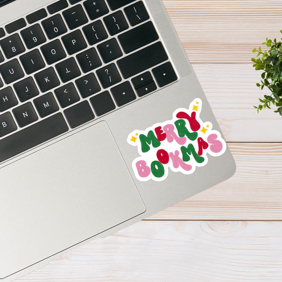 Laptop with a 'Merry Bookmas' sticker on a wooden surface