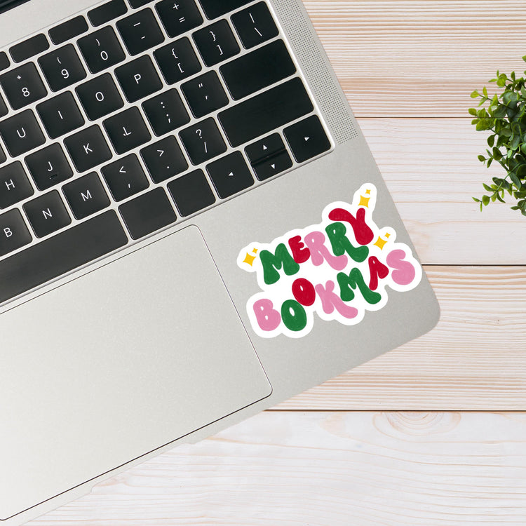 Laptop with a 'Merry Bookmas' sticker on a wooden surface