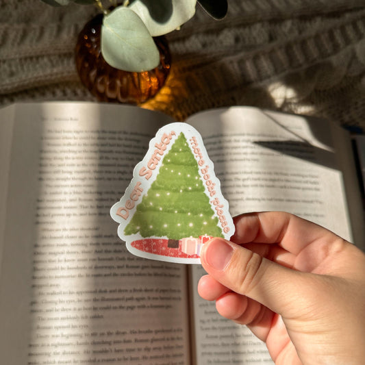 Hand holding a Christmas tree sticker over an open book with a warm glow.